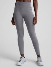woman wearing gray high-waisted long length leggings on a plain background.